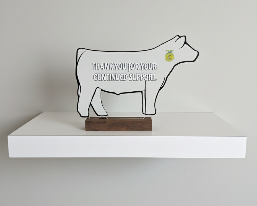 Decorative cow figure with a message on a white shelf against a gray wall